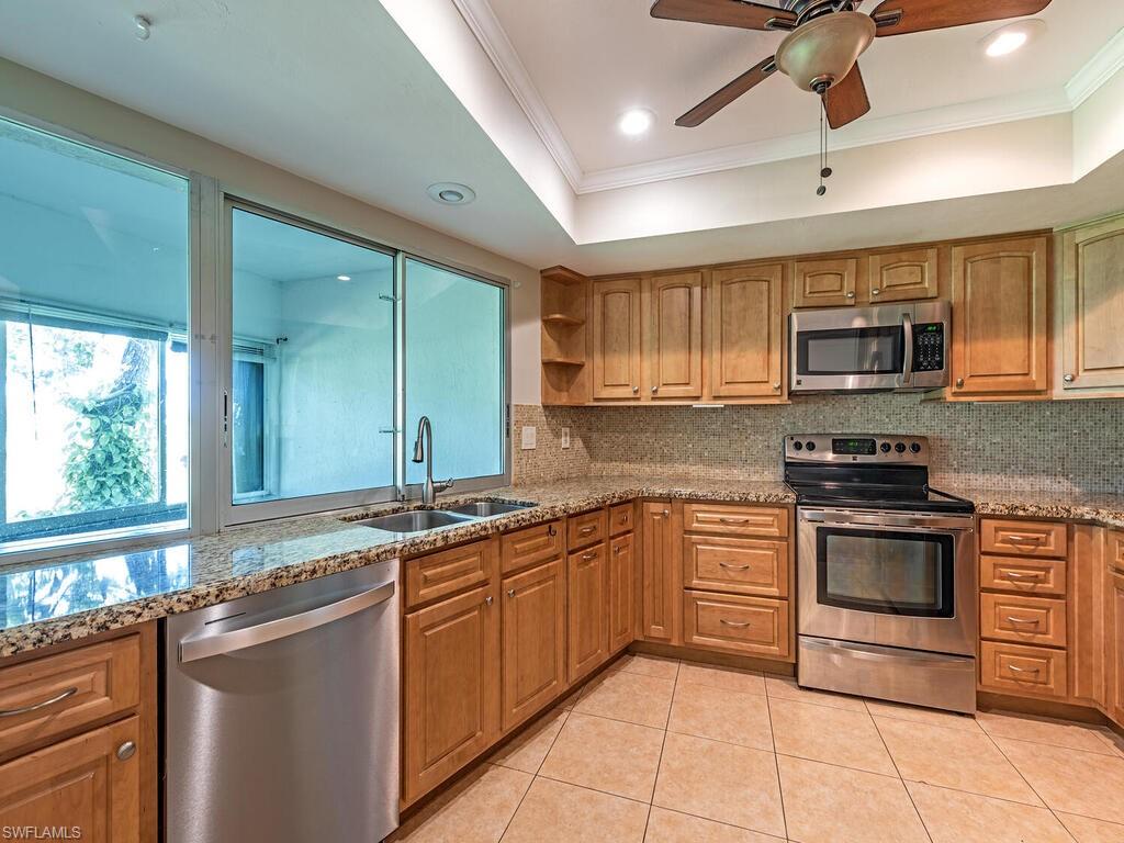 130 Round Key Circle, Unit G10 Naples, FL 34112 - Photo 6 of 12 a kitchen with stainless steel appliances granite countertop a stove top oven a sink dishwasher a dining table and chairs with wooden floor