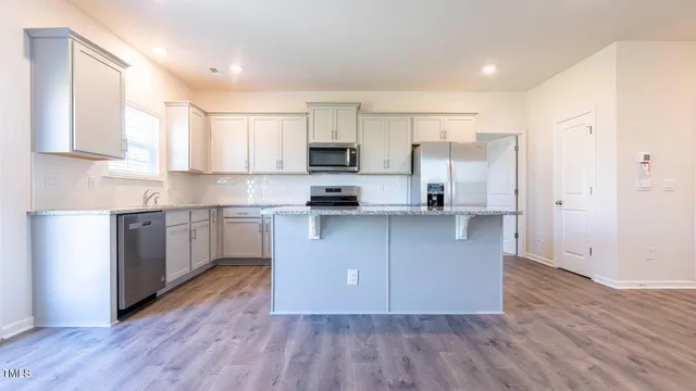 a kitchen with wooden floors white cabinets appliances and window