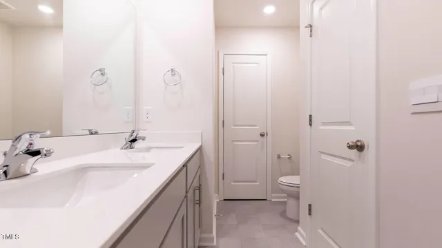 a spacious bathroom with a double vanity sink a mirror and a toilet