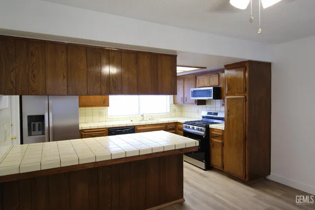 a kitchen with stainless steel appliances granite countertop a refrigerator a sink dishwasher a stove and black cabinets with wooden floor