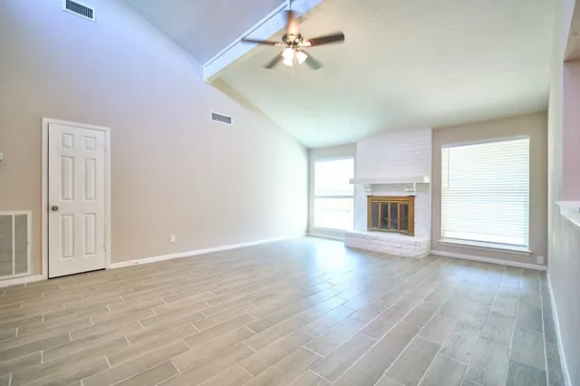 an empty room with wooden floor fireplace and windows