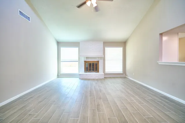 an empty room with wooden floor fireplace and windows