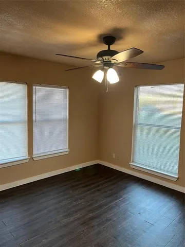 an empty room with wooden floor fan and windows