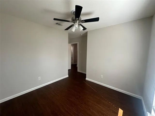 a view of an empty room with wooden floor and a ceiling fan