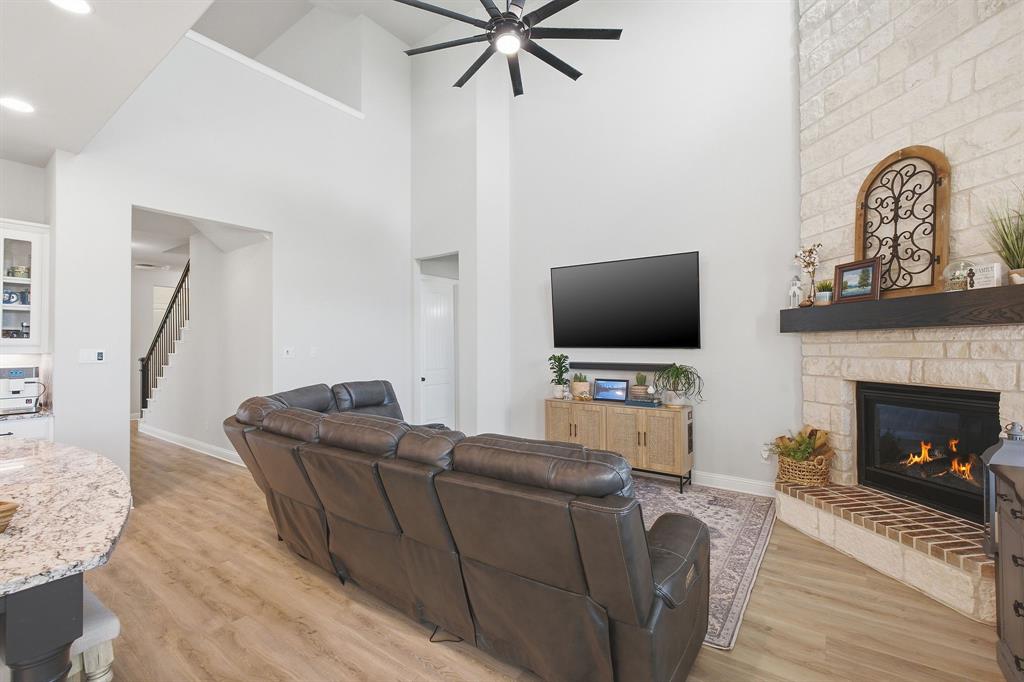 313 Tate Lane Anna, TX 75409 - Photo 9 of 30 Living area featuring a high vaulted ceiling with a ceiling fan, a fireplace with a light-colored brick surround and a dark wood mantel, and wood-finish flooring