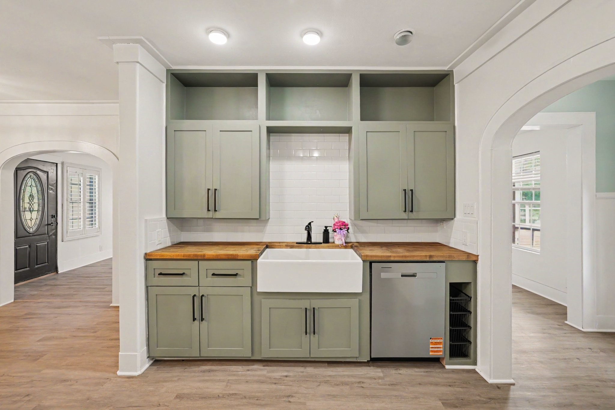 31730 Waller Tomball Road Waller, TX 77484 - Photo 14 of 50 This kitchen features a farmhouse sink, light green cabinets, and butcher block countertops, complemented by a subway tile backsplash. It includes a modern dishwasher with an open archway leading to mud room.