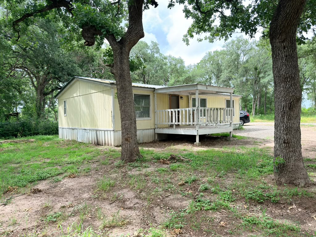 8607 Burleson Manor Road, Unit A Manor, TX 78653 - Photo 9 of 13 A quaint yellow home is nestled amongst mature trees, offering a private outdoor space.