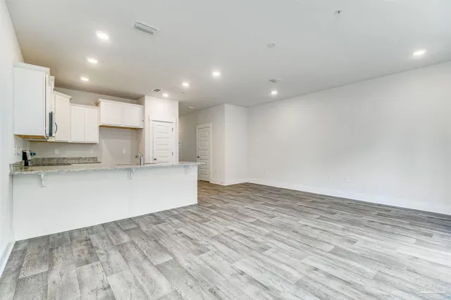 a large kitchen with stainless steel appliances granite countertop a stove a sink and white cabinets with wooden floor