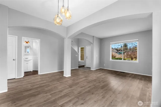 an empty room with wooden floor chandelier and windows