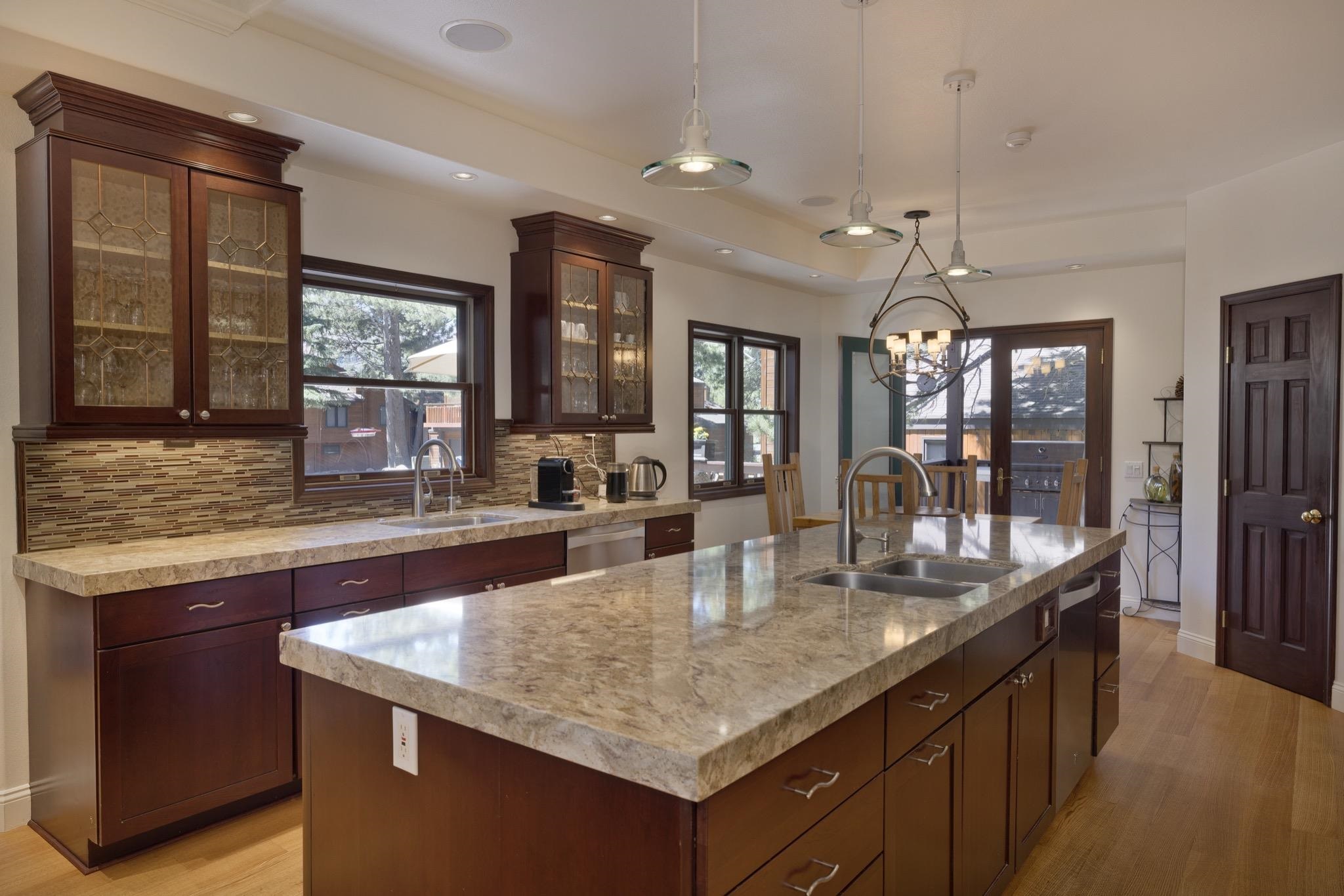 378 Ridge Way Mammoth Lakes, CA 93546 - Photo 11 of 43 Kitchen featuring a large island with an integrated double sink, wood-finish flooring, cherry-toned cabinetry, light-toned countertops, and mosaic tile backsplash