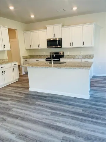 a view of kitchen with stainless steel appliances granite countertop a stove a sink and white cabinets