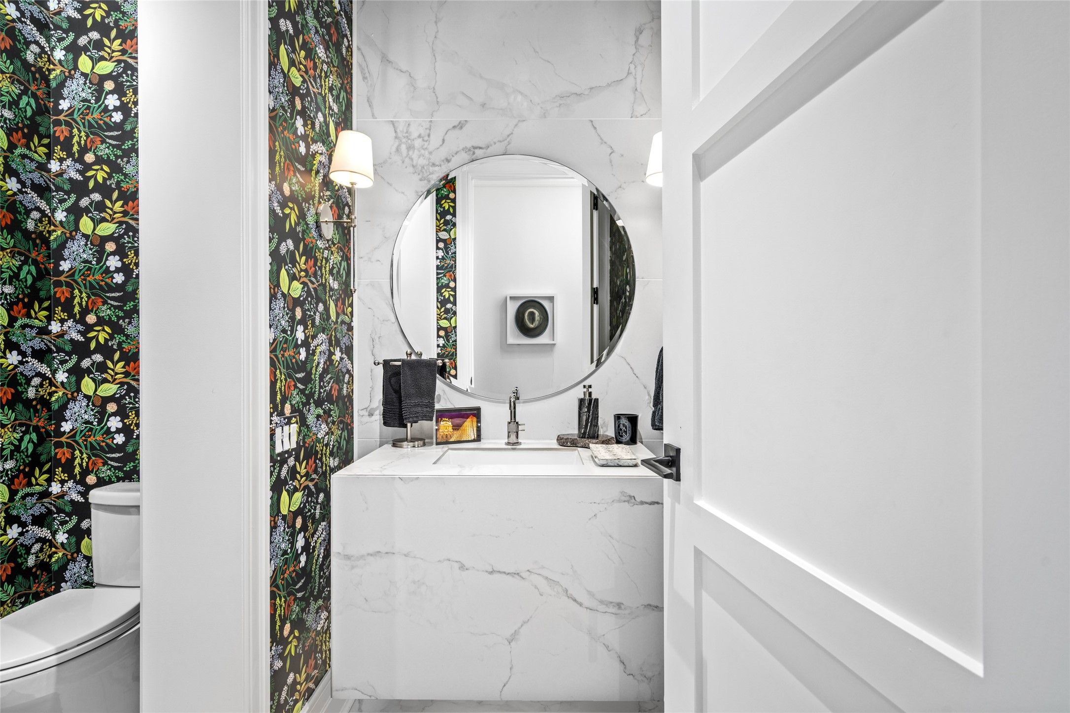 6017 Memorial Drive, Unit 202 Houston, TX 77007 - Photo 20 of 36 This chic powder room features porcelain tile floors and accent wall, a backlit floating vanity paired with a circular beveled mirror, chrome fixtures with shaded chrome sconces, and stylish decorative wallpaper for an eye catching elegant focal point.
