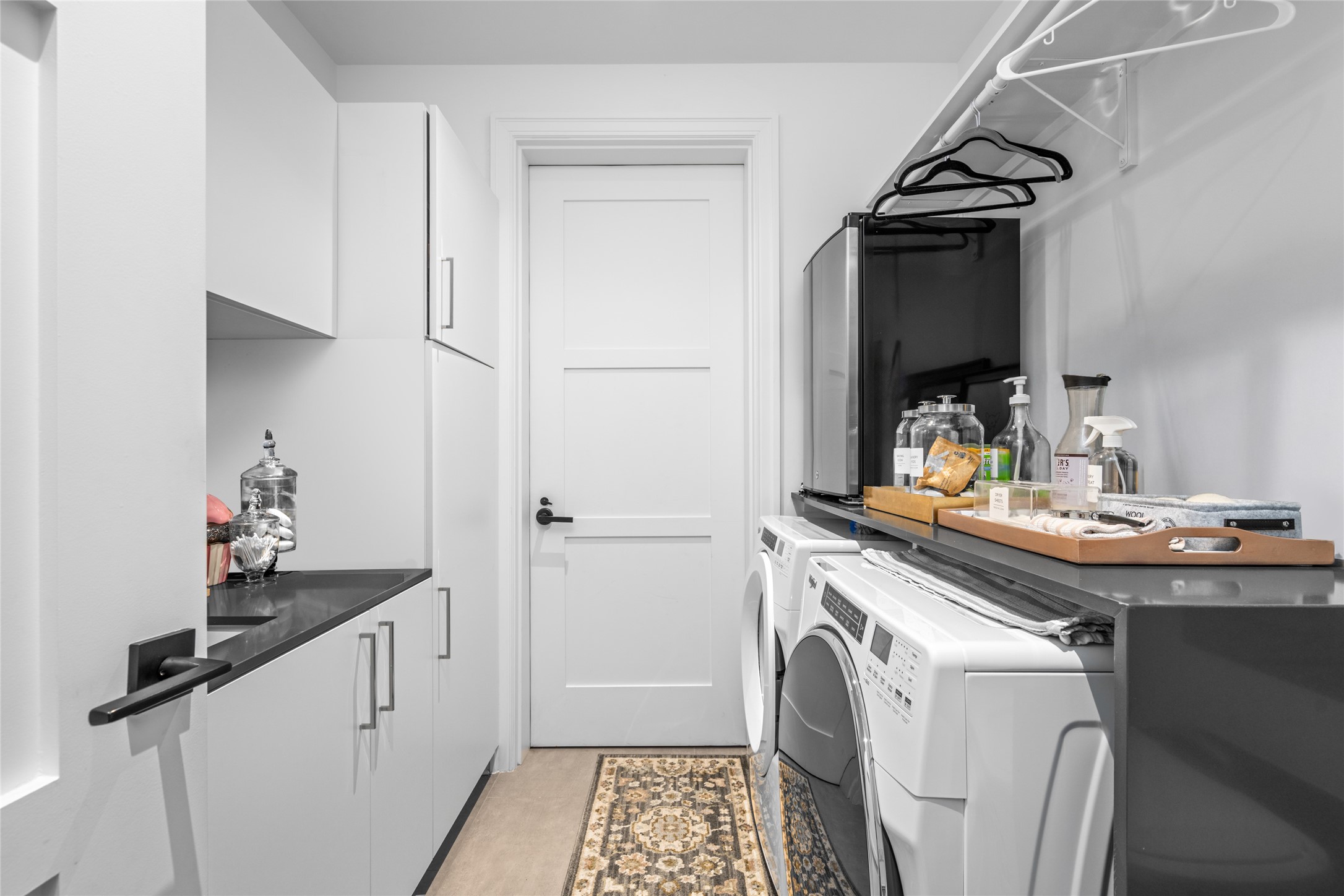 6017 Memorial Drive, Unit 202 Houston, TX 77007 - Photo 28 of 36 Equipped with a Whirlpool washer and dryer, a sink with gray quartz counters, a hanging rack, generous storage space, and a conveniently positioned backdoor leading directly to the trash chute - This utility room was built with purpose.
