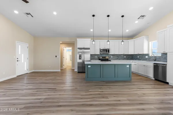 a kitchen with stainless steel appliances granite countertop a stove top oven a sink dishwasher a refrigerator and white cabinets with wooden floor