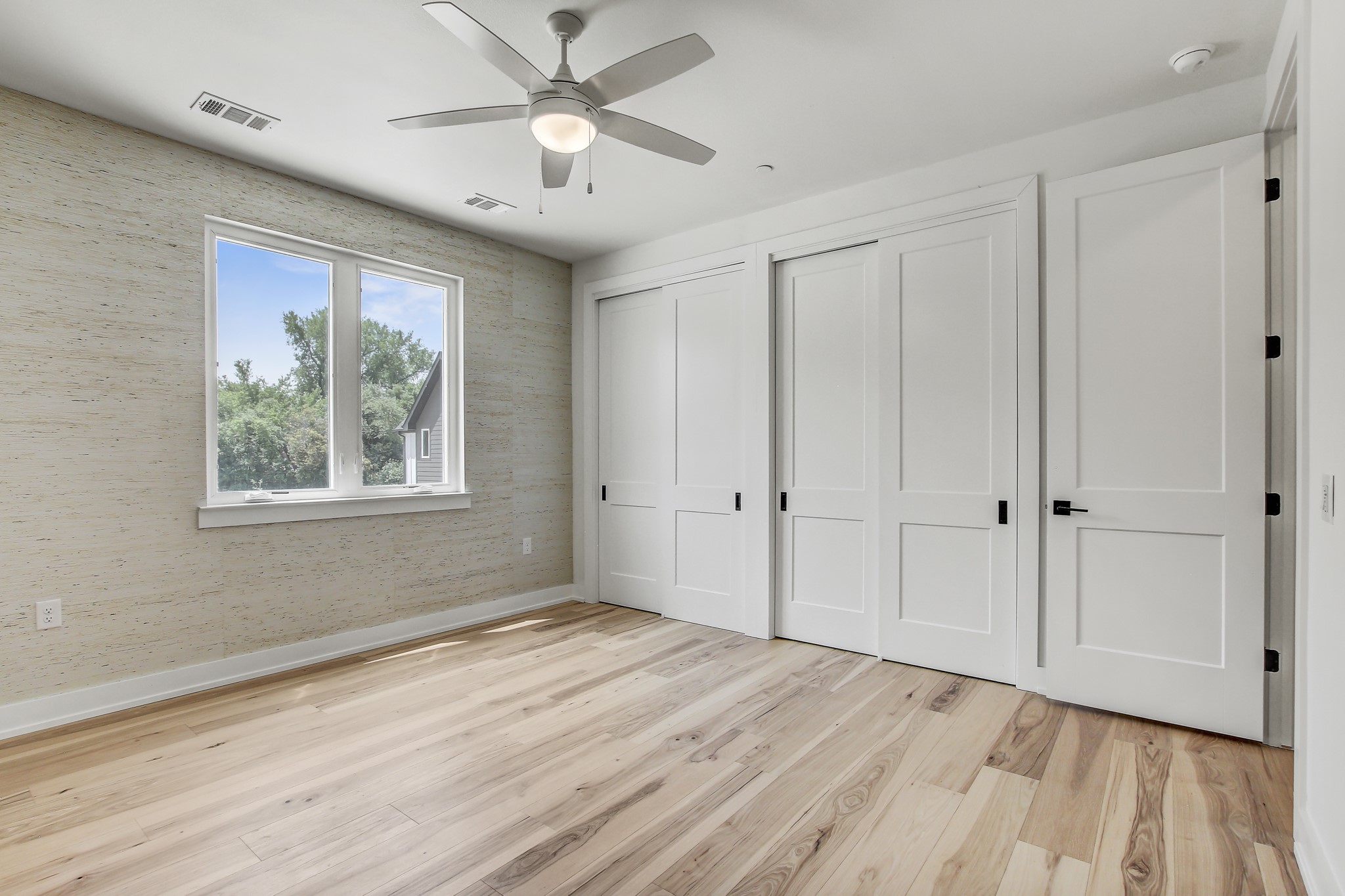 4127 East 12th Street, Unit 4 Austin, TX 78721 - Photo 14 of 32 Unfurnished bedroom featuring two closets, light wood-style floors, baseboards, ceiling fan, and wallpapered walls