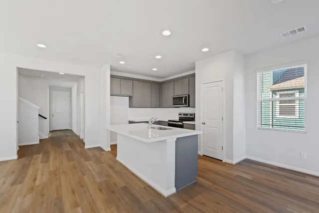 a kitchen with stainless steel appliances granite countertop a stove top oven a sink a refrigerator and white cabinets with wooden floor