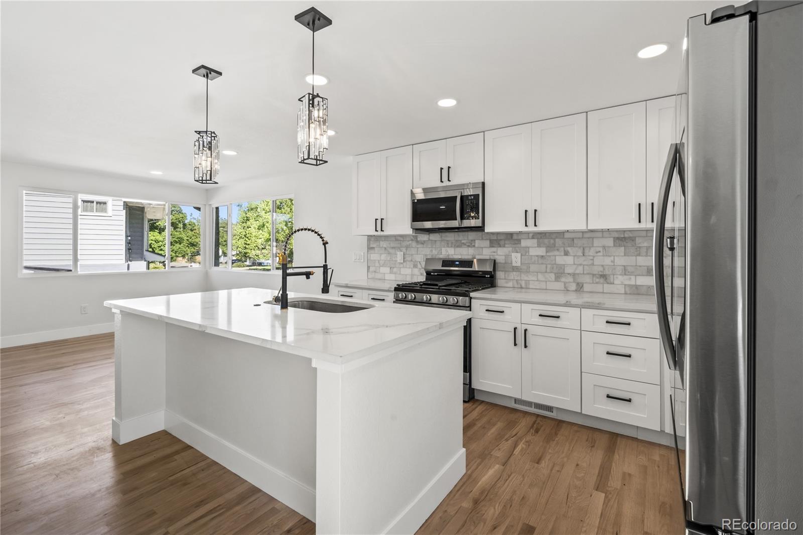 3495 Miller Street Wheat Ridge, CO 80033 - Photo 6 of 40 a kitchen with kitchen island white cabinets a sink a window and appliances