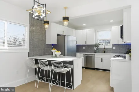 a kitchen with stainless steel appliances granite countertop a stove top oven a refrigerator a sink and a dining table with white cabinets