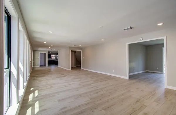 an empty room with wooden floor and way to kitchen