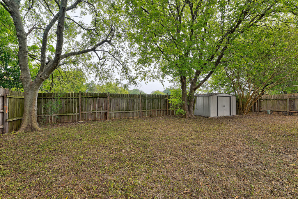 6002 Baton Rouge Drive Austin, TX 78727 - Photo 18 of 20 Expansive backyard featuring mature trees, a wood privacy fence, and a metal storage shed