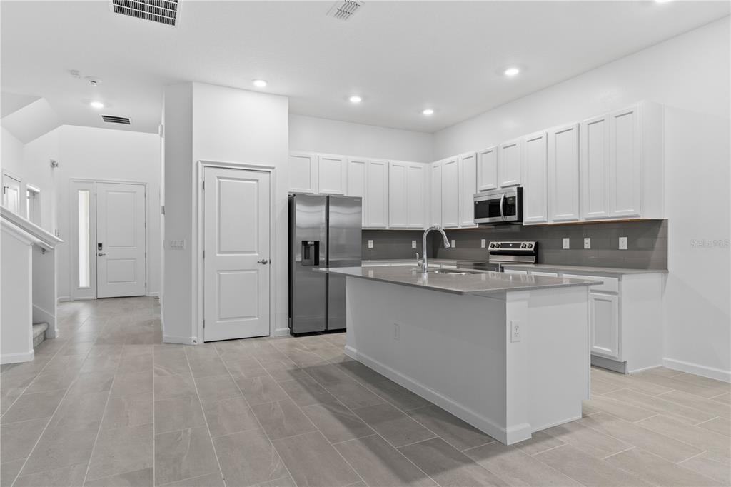 1205 Butterfly Orchid Road Davenport, FL 33837 - Photo 8 of 69 a kitchen with stainless steel appliances granite countertop a refrigerator sink and white cabinets