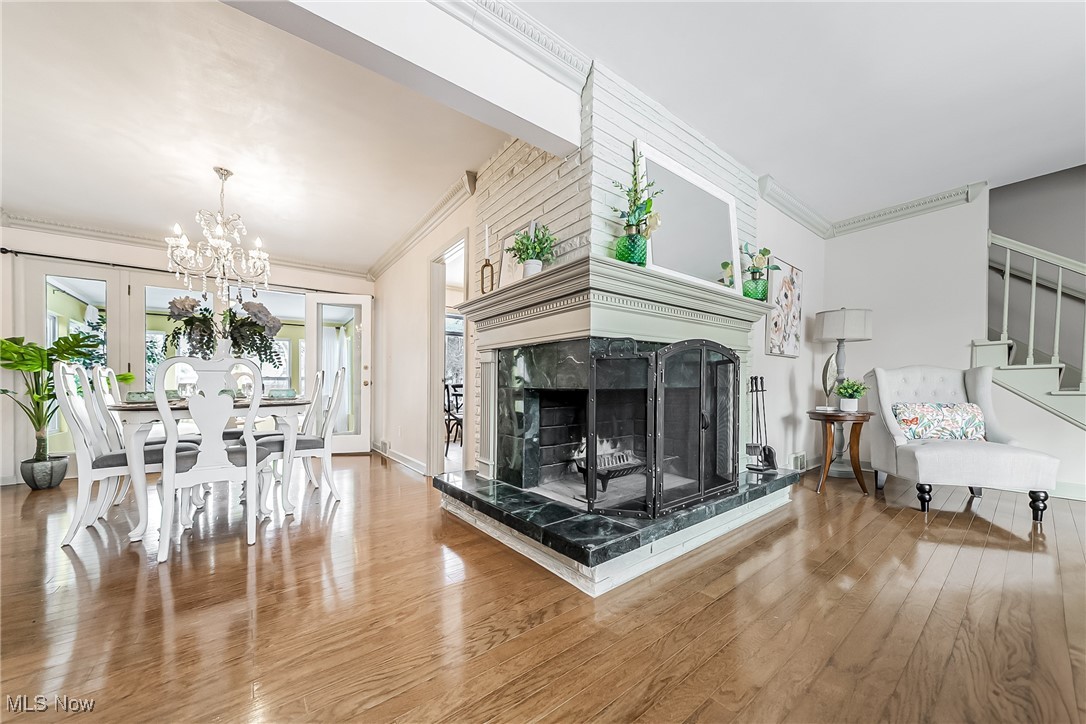 Living room with a fireplace, hardwood floors, crown molding, and an inviting chandelier