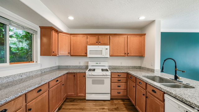 U-shaped kitchen featuring wood cabinetry, speckled countertops, stainless steel double basin sink with a matte black faucet, and a built-in white microwave