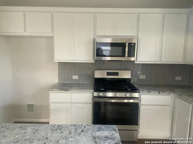 a kitchen with stainless steel appliances granite countertop a stove a microwave and a white cabinets