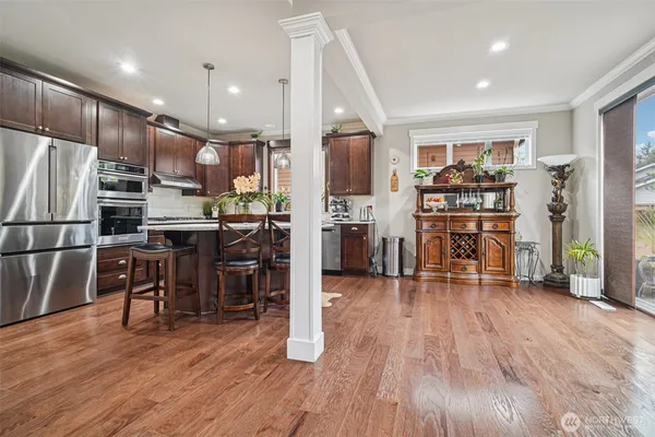 a living room with stainless steel appliances furniture wooden floor and a kitchen view