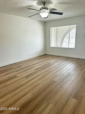 an empty room with wooden floor chandelier fan and windows