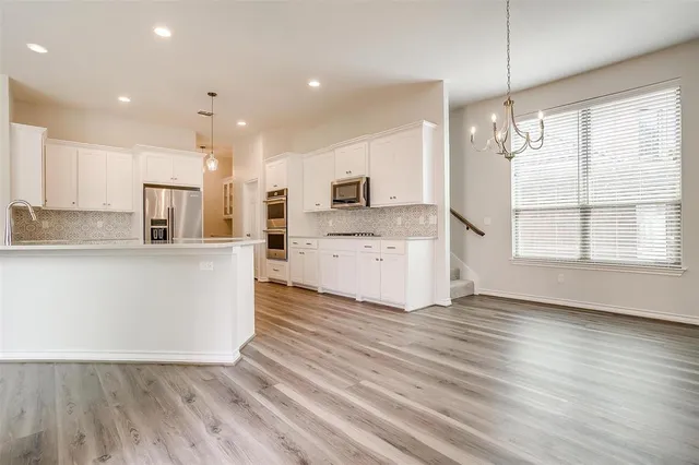 a large kitchen with stainless steel appliances granite countertop a refrigerator a oven a sink and white cabinets with wooden floor