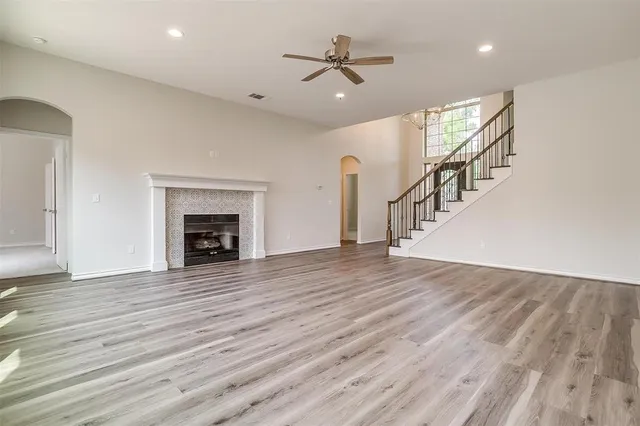 a view of an empty room with wooden floor a ceiling fan and a fireplace