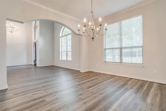 an empty room with wooden floor chandelier and windows