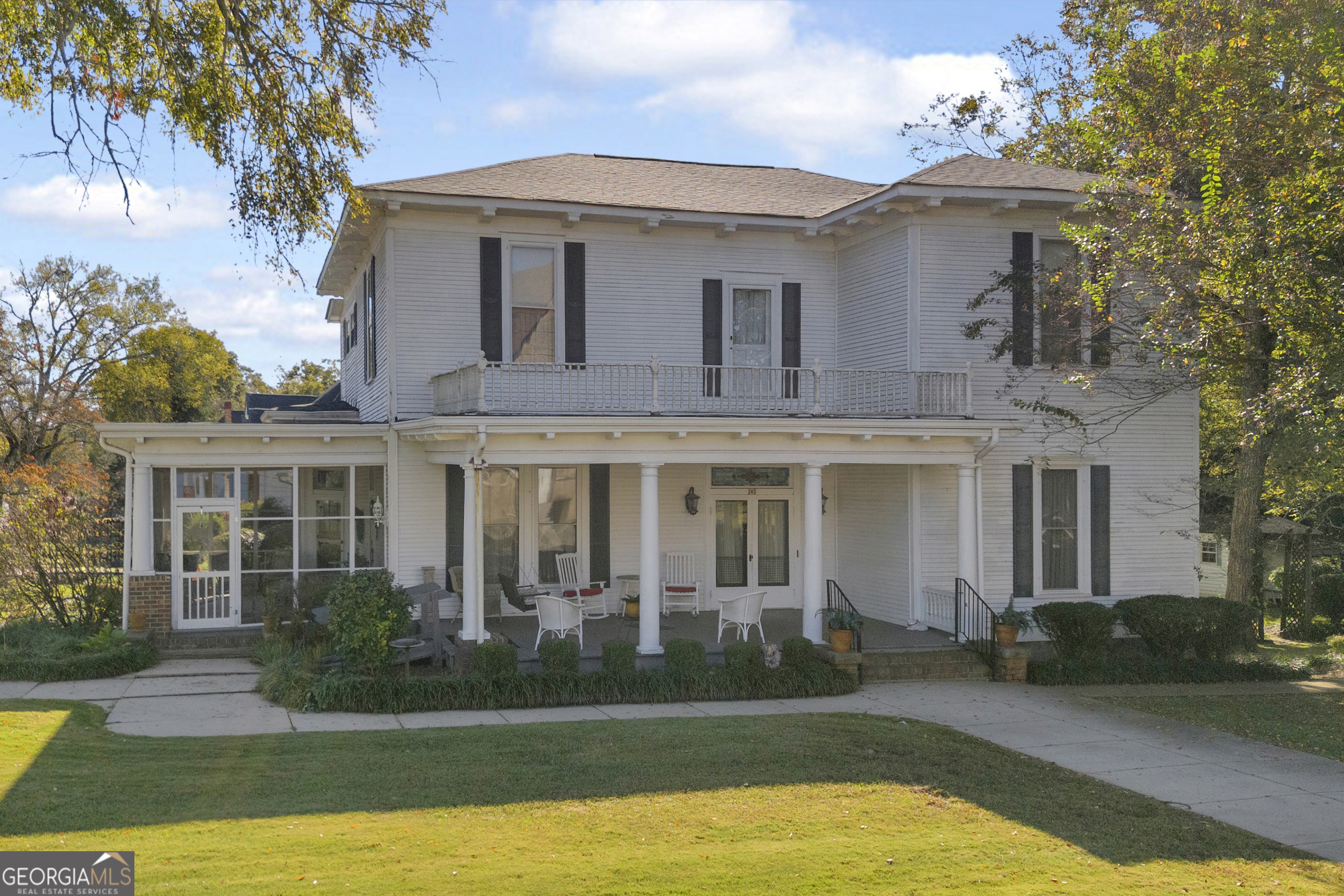 a view of a white house with a large windows and a yard with plants and large trees