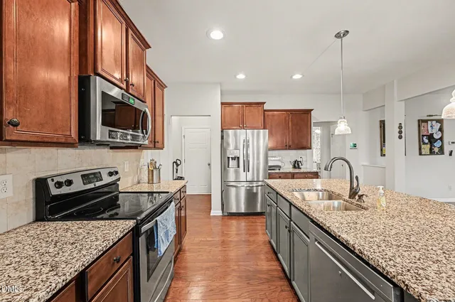 a kitchen with stainless steel appliances granite countertop a stove top oven a refrigerator a dining table and chairs with wooden floor