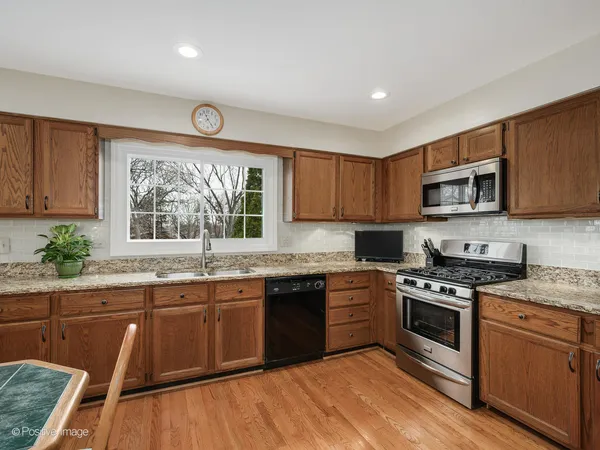 a kitchen with stainless steel appliances granite countertop wooden cabinets a sink a stove a microwave and wooden floors
