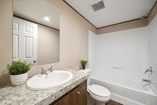 a bathroom with a granite countertop sink a toilet a mirror and shower