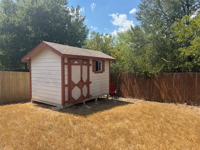 a view of a small barn in front of a house with wooden fence