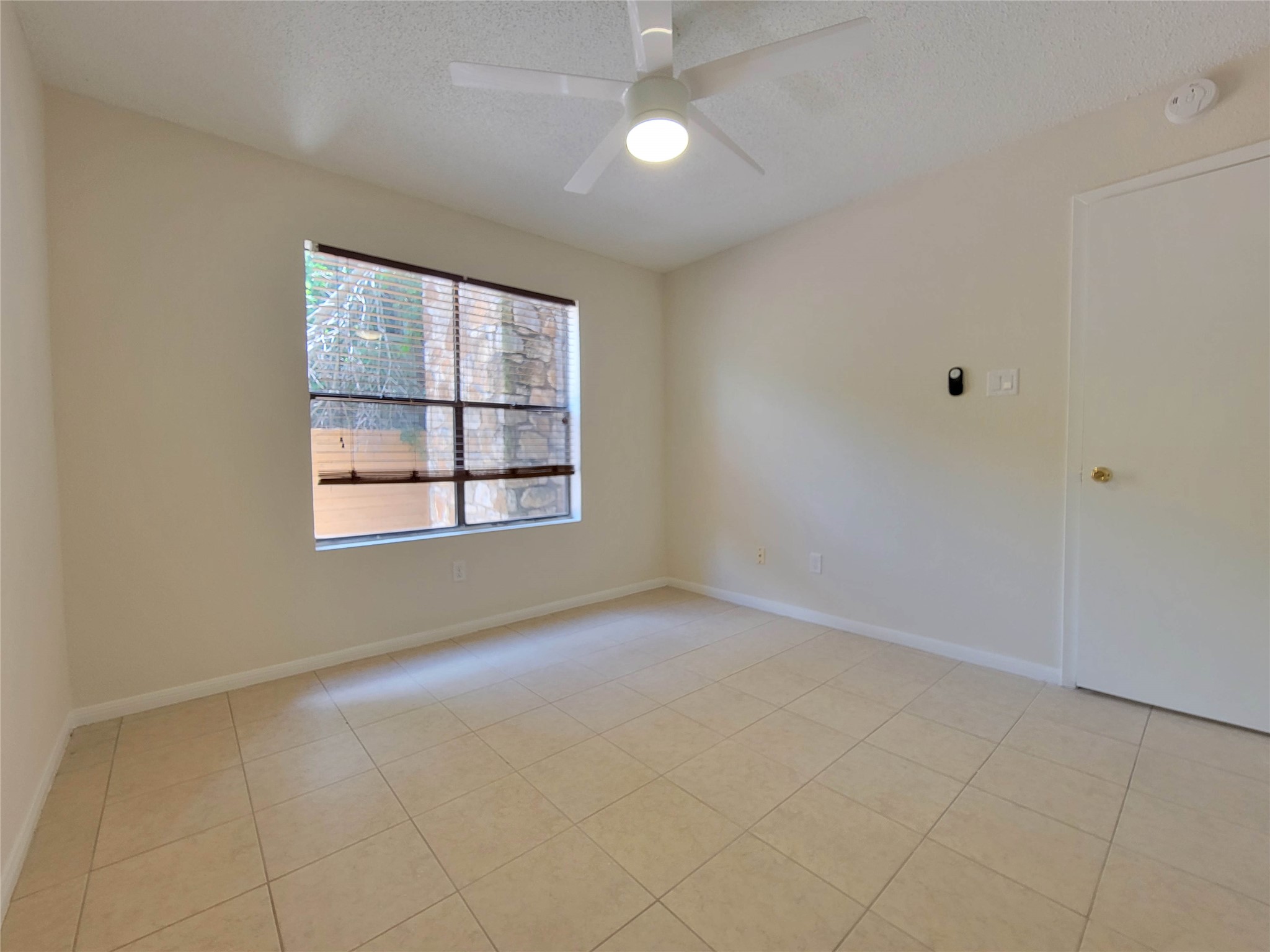 8706 Schick Road, Unit A Austin, TX 78729 - Photo 24 of 33 A well-lit bedroom with tiled floors and a ceiling fan, offering a serene personal retreat.