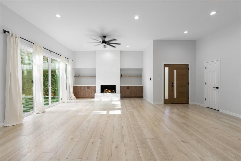 14140 Regency Place Dallas, TX 75254 - Photo 4 of 38 Spacious living area featuring light wood-finish flooring, a white brick fireplace with a hearth, and built-in cabinetry with open shelving