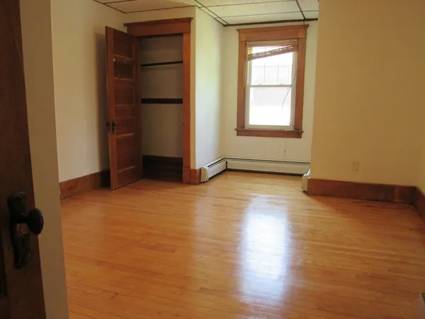 an empty room with wooden floor closet and windows