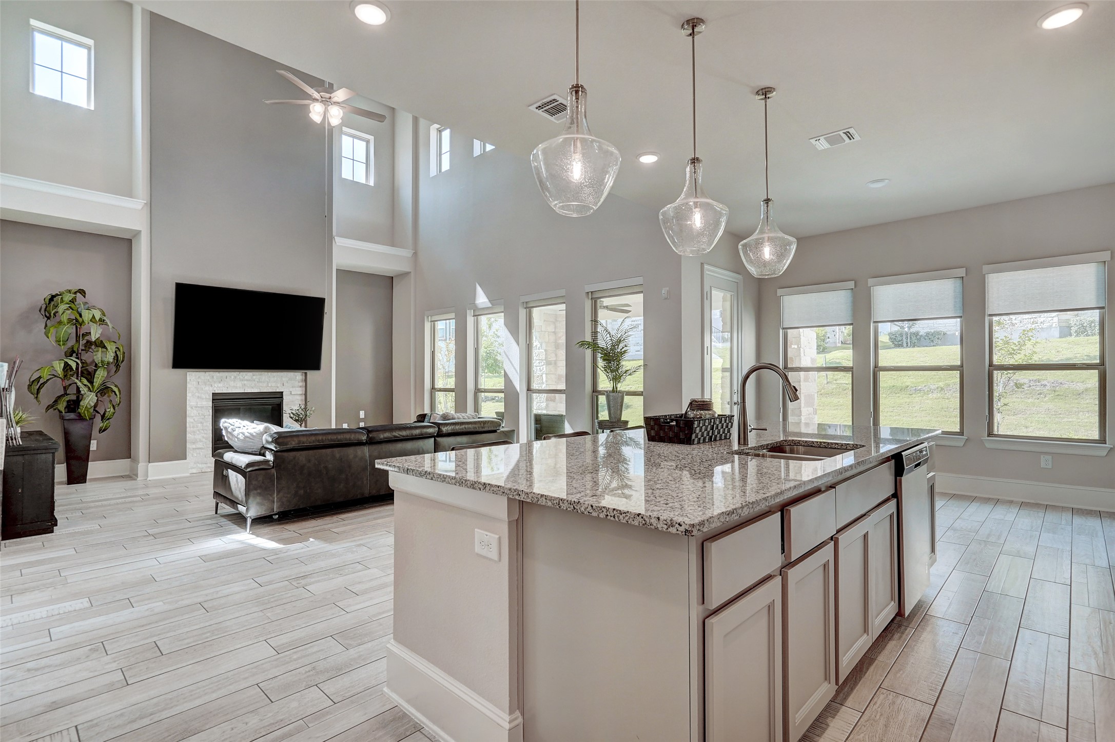 720 Rawson Bend Austin, TX 78738 - Photo 11 of 39 Kitchen with light stone counters, a stone fireplace, a center island with sink, pendant lighting, and wood finish floors