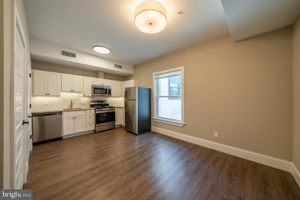 a kitchen with granite countertop a stove a sink dishwasher a refrigerator and white cabinets with wooden floor