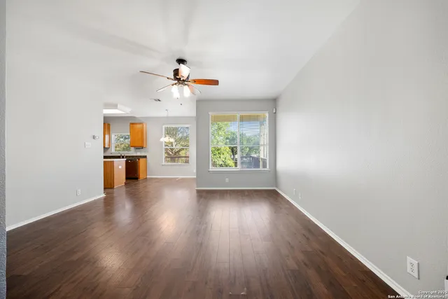 an empty room with wooden floor chandelier fan and windows
