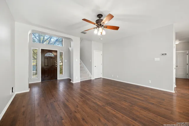 a view of an empty room with wooden floor and a ceiling fan