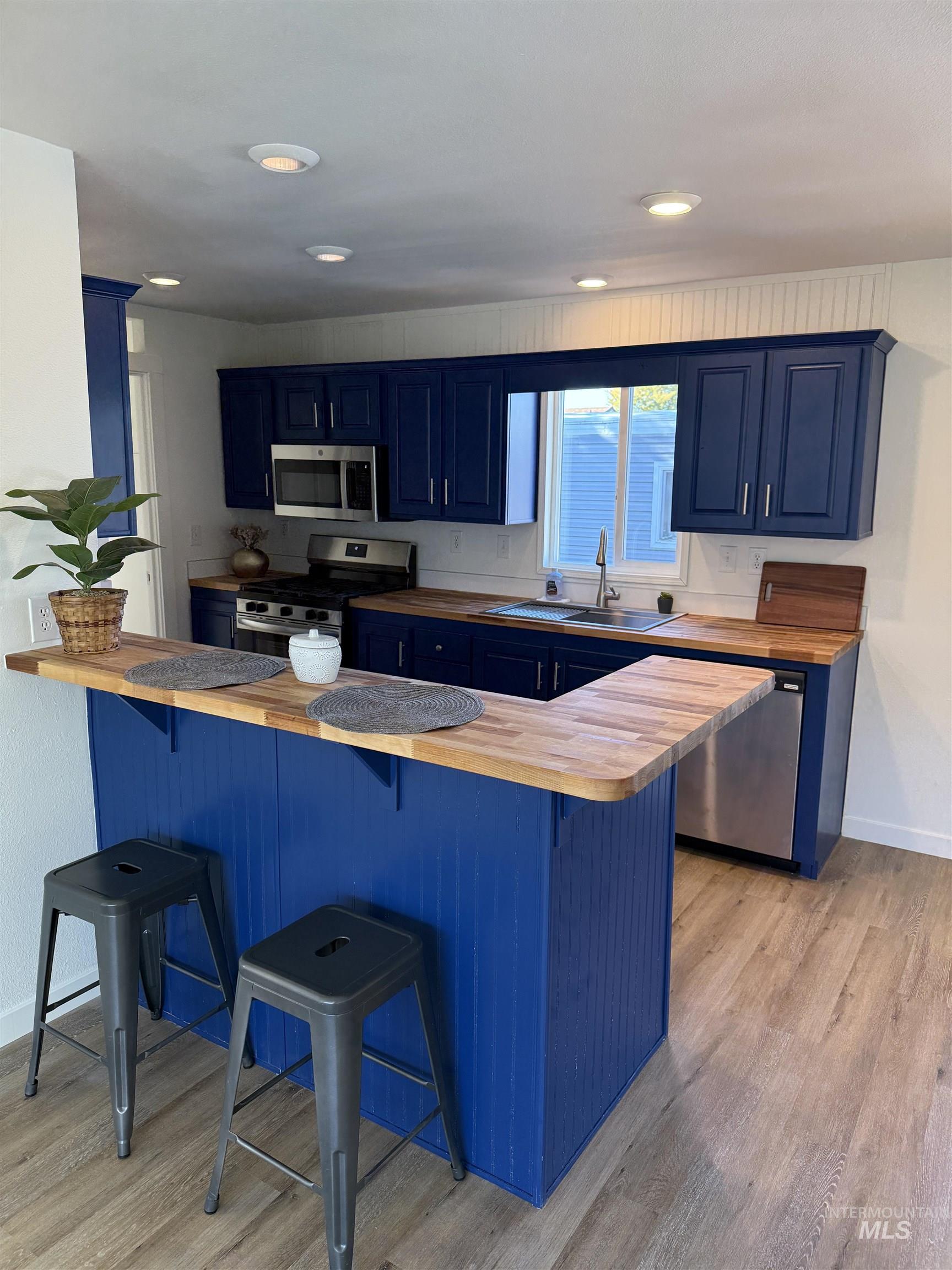 Kitchen featuring blue cabinetry, a breakfast bar area, stainless steel appliances, light wood-style floors, and recessed lighting