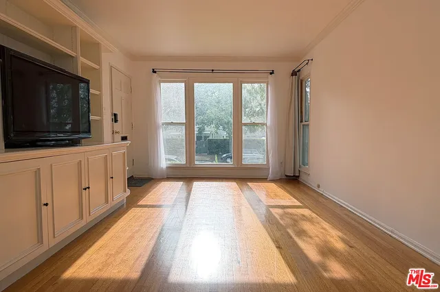 a view of an empty room with window and a kitchen view