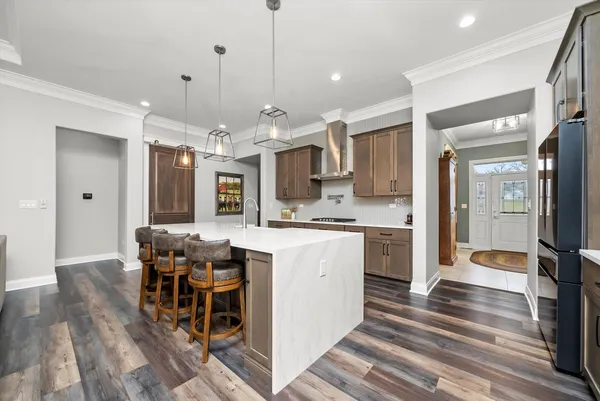 a kitchen with stainless steel appliances kitchen island granite countertop a stove top oven a sink dishwasher a refrigerator and white cabinets with wooden floor