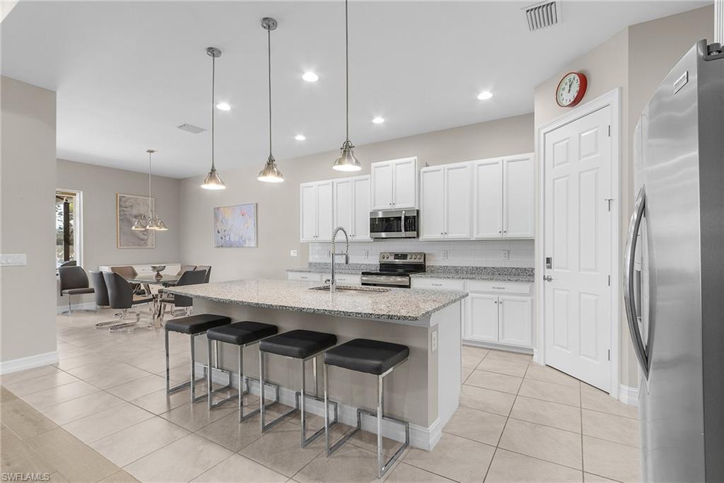 14539 Kelson Circle Naples, FL 34114 - Photo 7 of 37 Kitchen with appliances with stainless steel finishes, an island with sink, pendant lighting, light stone counters, and a breakfast bar area