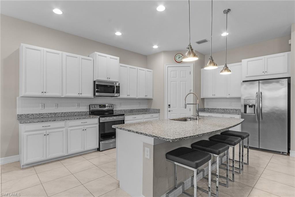 14539 Kelson Circle Naples, FL 34114 - Photo 8 of 37 Kitchen with stainless steel appliances, a breakfast bar area, hanging light fixtures, white cabinetry, and light tile patterned floors